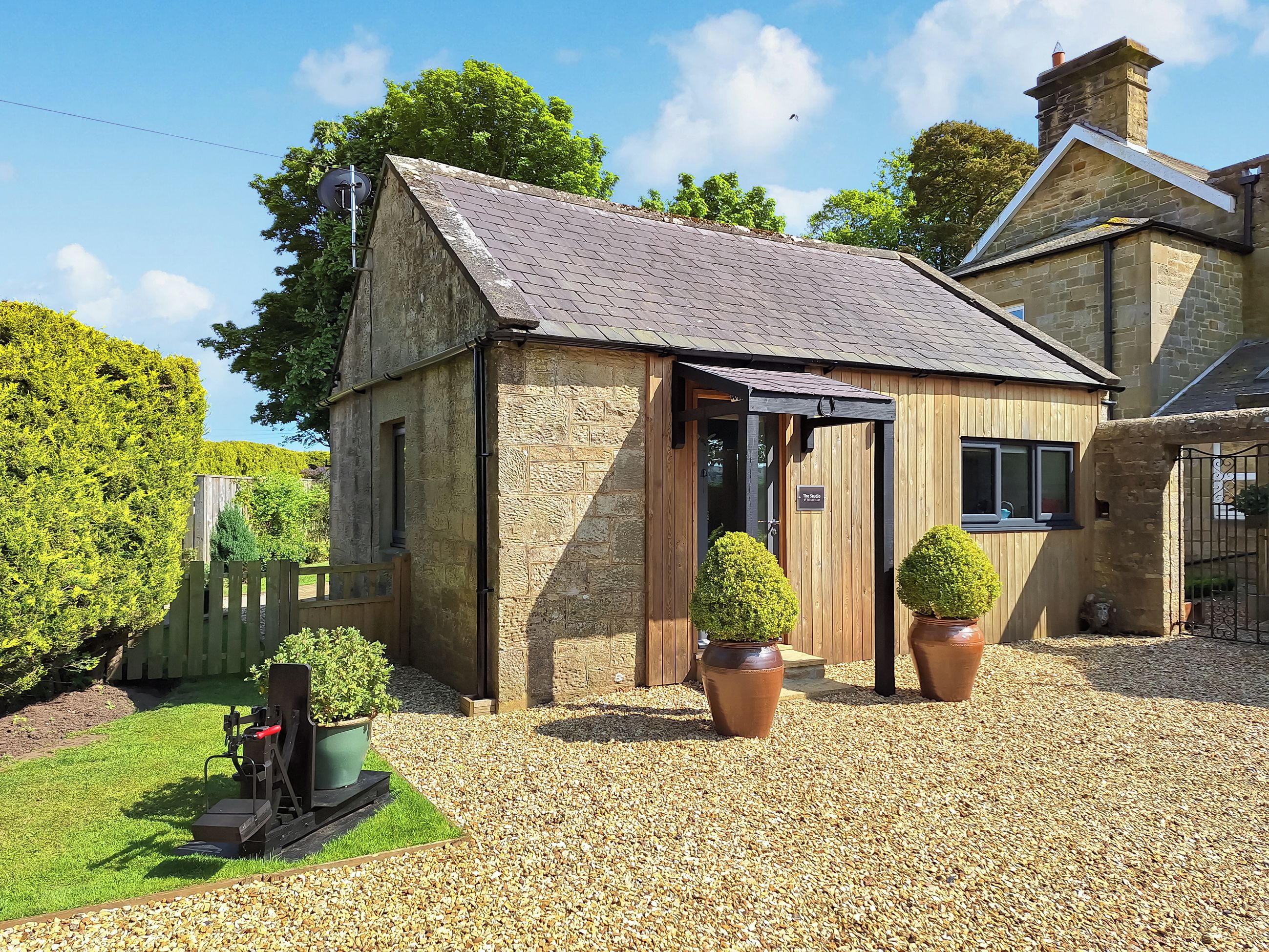 A stone building with a sloped roof, a wooden door, and two potted plants.