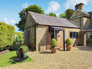 A stone building with a sloped roof, a wooden door, and two potted plants.