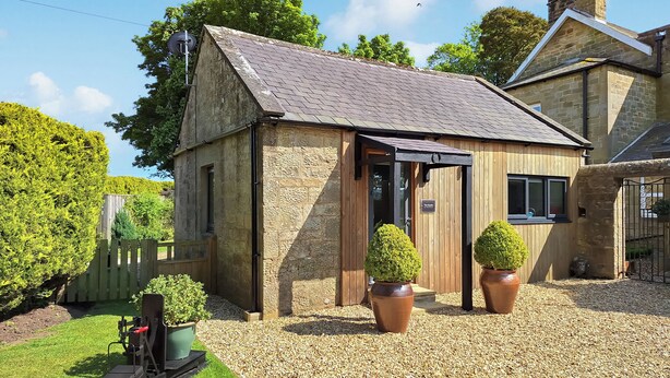 A stone building with a sloped roof, a wooden door, and two potted plants. - The Studio at Westfield (Bellingham, near Hexham)