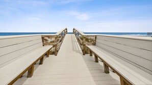 Ein hölzerner Gehweg führt zum Strand, gesäumt von Bänken.