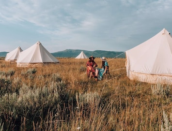 Two campers visiting in the field with mountains views outside of our waterproof, canvas bell tents with low profile windows and large netted, double zipper doors at our Yellowstone camp.