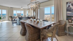 A spacious dining area with a large wooden table, wicker chairs, and a chandelier. - Emerald Isle 108 Beach Front First Floor End Unit (Pensacola Beach)