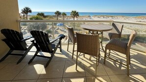 A balcony with a view of the beach, featuring black chairs, wicker chairs, and a small round table. - Emerald Isle 108 Beach Front First Floor End Unit (Pensacola Beach)