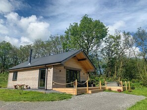 A wooden cabin with a sloped roof, a chimney, and a porch with a rope barrier.