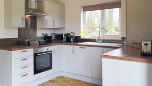 A modern kitchen with white cabinets, a built-in oven, a microwave, a kettle, and a sink under a window. - 2 bedroom accommodation in Cwrt Newydd, near Llandysul (Cwrt Newydd, near Llandysul)