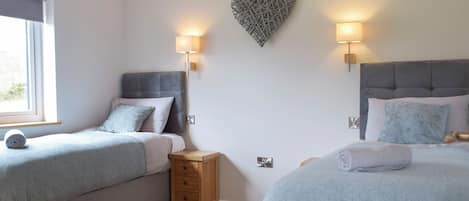 A bedroom with two beds, a heart-shaped wall decoration, and bedside lamps.