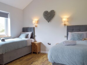 A bedroom with two beds, a heart-shaped wall decoration, and bedside lamps.