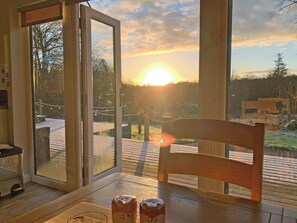 A room with a wooden table, a chair, and a view of the sunset through a glass door.