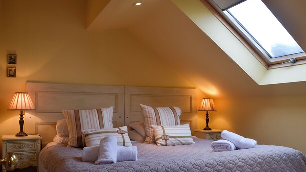 A bedroom with a high ceiling and skylight, featuring a large bed with multiple pillows and two bedside lamps. - Fennel Folly - UK32608 (Manton, near Oakham)