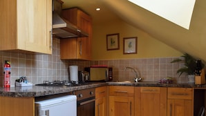 A kitchen with wooden cabinets, a microwave, a sink, and a stove. - Fennel Folly - UK32608 (Manton, near Oakham)