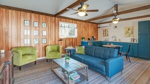 A cozy living room with a blue sofa, green armchairs, and a coffee table. There is a kitchen area with blue cabinets and a window. - 10 minutes to Asheville, Biltmore Estate, hike and bike trails (Fairview)