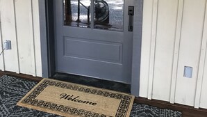 Une porte d’entrée avec un panneau de verre, un paillasson sur lequel est écrit « Bienvenue », et une petite fenêtre au-dessus de la porte.