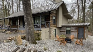 Un chalet rustique avec une façade en pierre, une véranda dotée de chaises en bois et une allée gravillonnée.