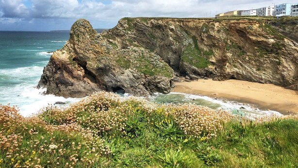 Un paysage côtier avec une falaise rocheuse, une plage et une rangée de bâtiments en arrière-plan.