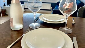Une table à manger dressée avec des assiettes, une bouteille et des verres, donnant sur la plage par une fenêtre.