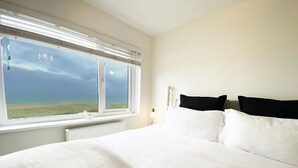 Une chambre avec un grand lit, une fenêtre donnant sur la mer et un radiateur placé sous la fenêtre.
