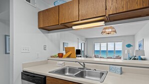 A modern kitchen with wooden cabinets, a stainless steel sink, and a view of the ocean through large windows. - Maritime West Unit C-33-Ocean Front Condo (Atlantic Beach)