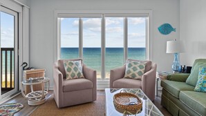 A living room with two armchairs, a green sofa, a glass coffee table, and a view of the ocean through large windows. - Maritime West Unit C-33-Ocean Front Condo (Atlantic Beach)