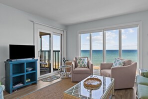 Ein Wohnzimmer mit Fernseher, zwei Sesseln, einem Couchtisch und Blick auf das Meer.