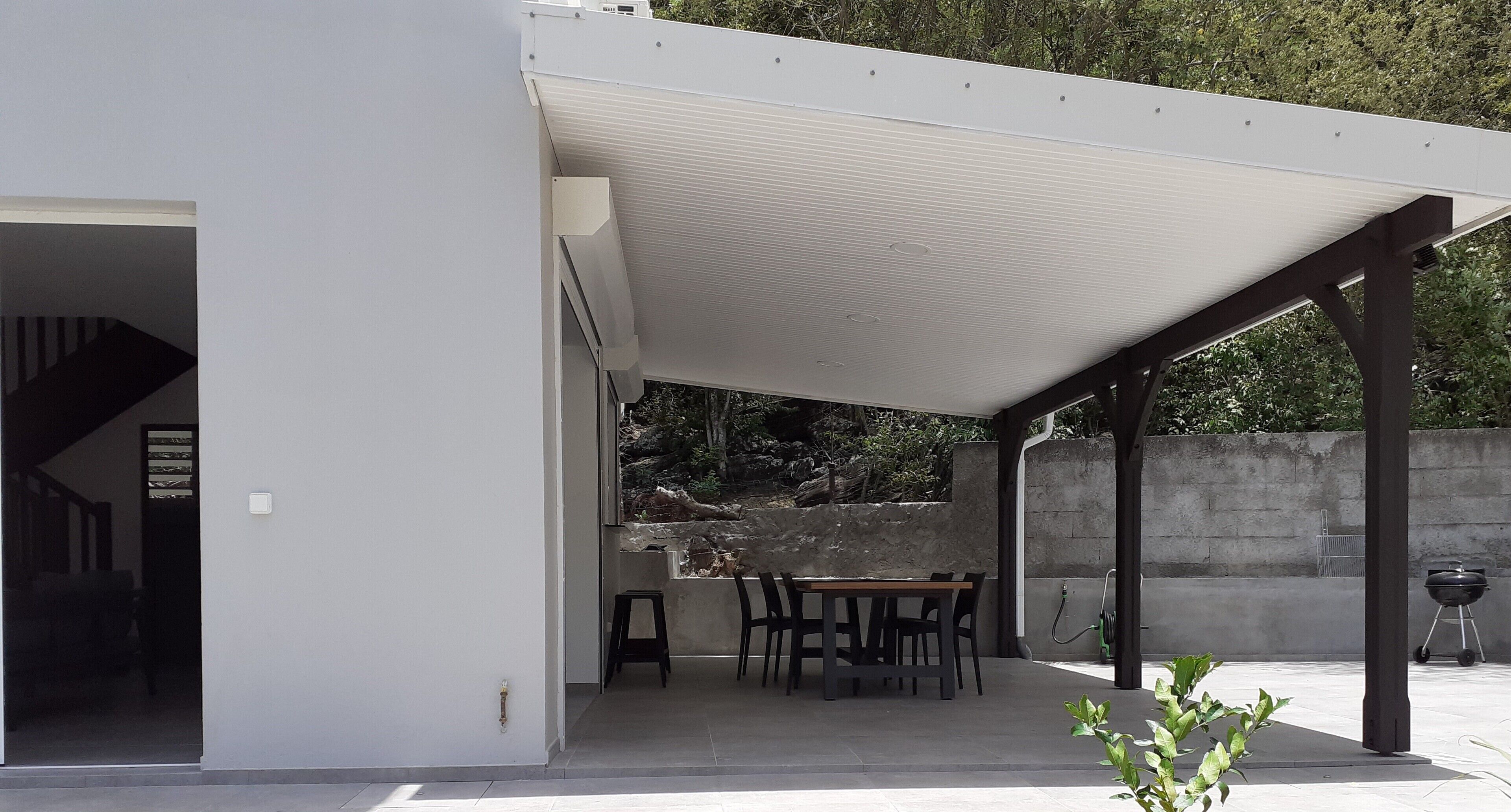 A covered patio area with a table and chairs, a grill, and a view of a natural landscape.