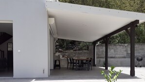 A covered patio area with a table and chairs, a grill, and a view of a natural landscape.