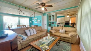 A living room with two beige sofas, a glass coffee table, and a ceiling fan.