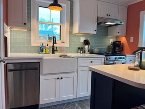 A kitchen with white cabinets, a stainless steel dishwasher, a stove, and a window with a view of the outside.