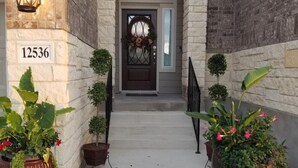 Entrada d'edifici residencial amb façana de maó, placa amb el número de l'adreça, porta principal fosca amb una corona decorativa i plantes en testos a ambdós costats de l'entrada.