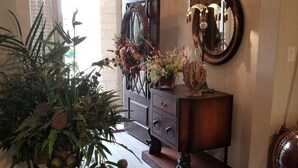 Un passadís ben il·luminat amb una planta gran en test, un mirall decoratiu i un moble prestatge amb un mirall a la part superior.