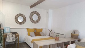 A bedroom with a bed, a desk, a chair, two wall-mounted mirrors, and a bedside table with a plant. - Studio Forêt (Amnéville)