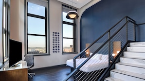 A modern hotel room with a large window, a flat-screen TV, a desk, and a staircase with a marble finish. - Courtyard by Marriott Cincinnati Downtown (Cincinnati)