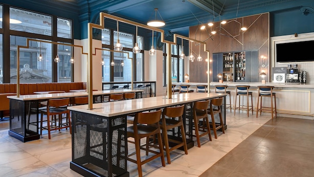 A modern bar area with high tables and stools, large windows, and a bar counter with a TV and coffee machine. - Courtyard by Marriott Cincinnati Downtown (Cincinnati)