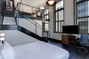 A modern hotel room with a large bed, a desk with a flat-screen TV, a chair, and a staircase leading to an upper level. - Courtyard by Marriott Cincinnati Downtown (Cincinnati)
