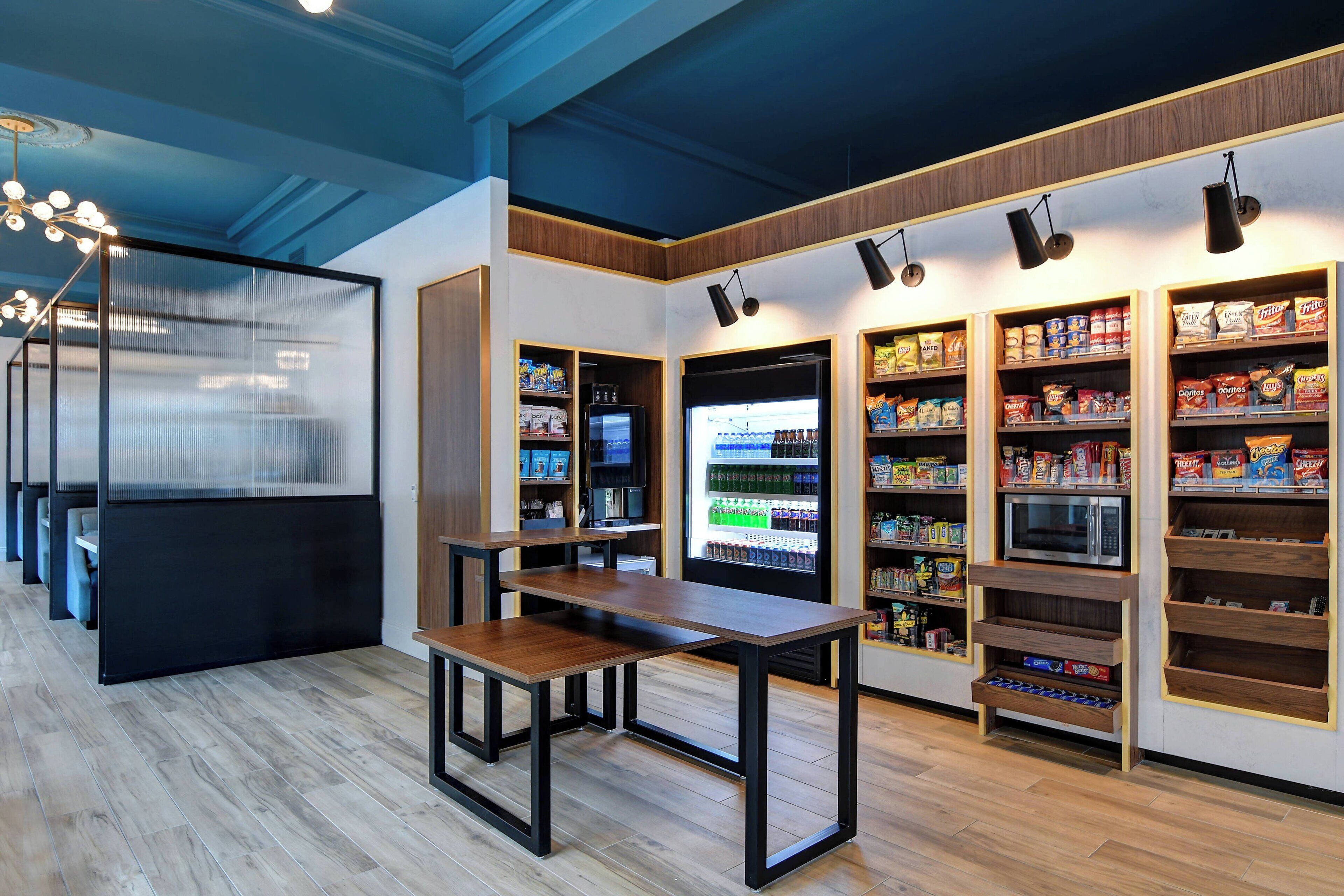 A modern interior with a wooden floor, a central table, and shelves stocked with snacks and beverages.