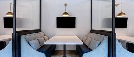 Una habitación moderna con una mesa central, dos zonas de estar con cojines y dos lámparas colgantes.