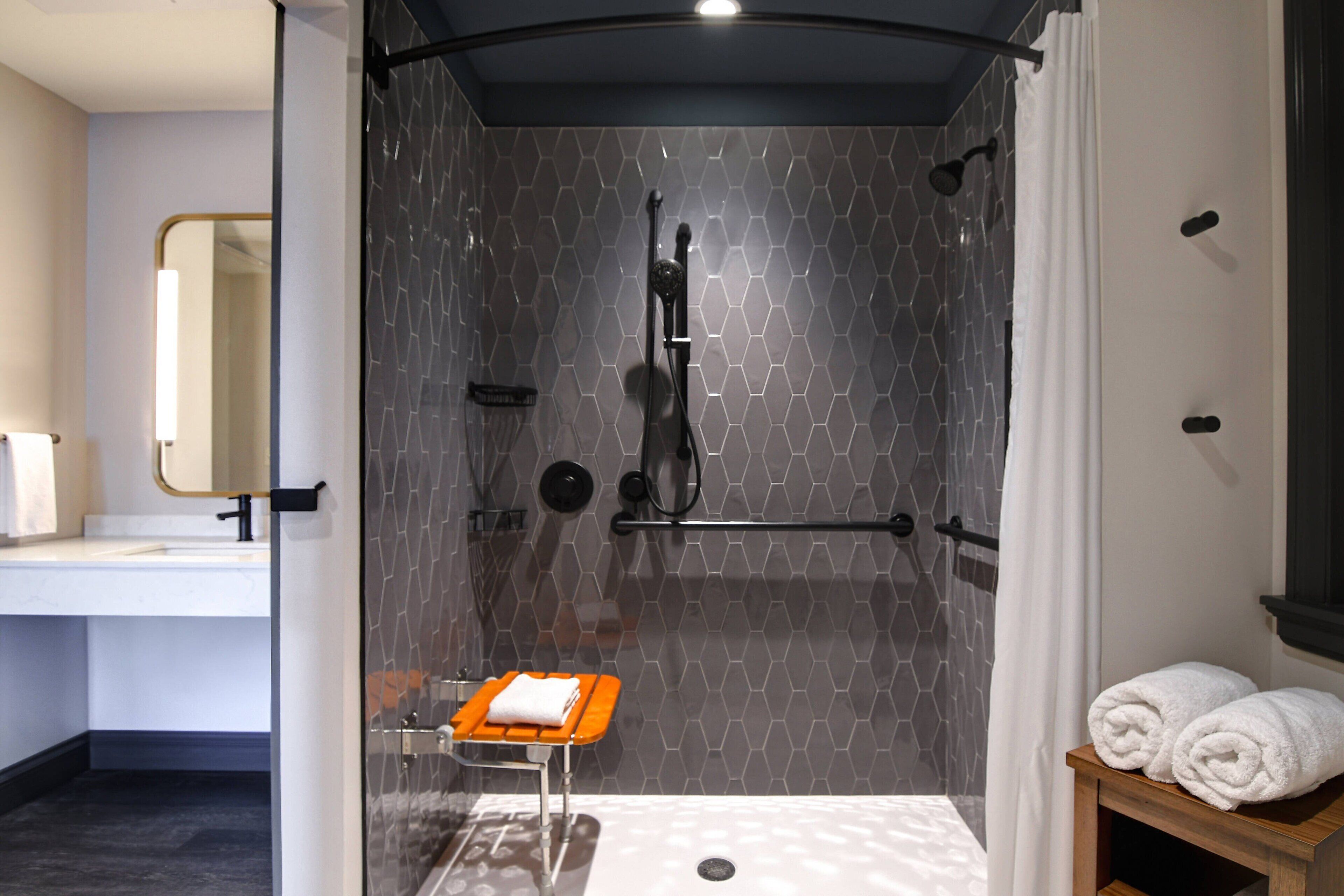 A modern bathroom with a glass-enclosed shower, a vanity with a mirror, and a wooden side table with towels.