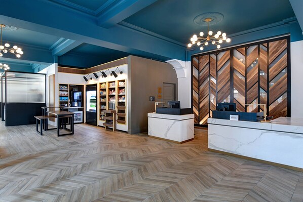 A modern hotel lobby with a herringbone wood floor, a reception desk, a seating area, and a wall with a chevron pattern. - Courtyard by Marriott Cincinnati Downtown (Cincinnati)