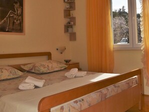 Ein Schlafzimmer mit einem hölzernen Bett, Kissen mit Blumenmuster, einem Nachttisch mit Lampe und einem Fenster mit Vorhängen.