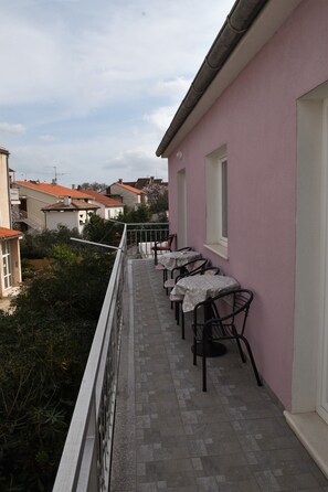 Ein Balkon mit Sitzgelegenheit, ein pinkfarbenes Gebäude und umgebende Vegetation.