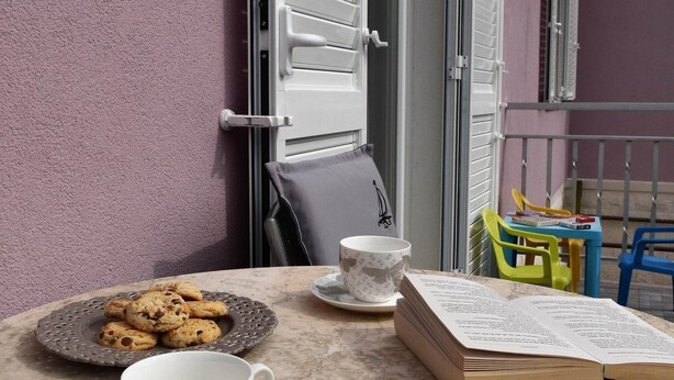 A balcony with a table set for tea, cookies, and an open book.