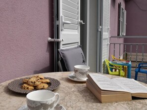 Un balcon avec une table préparée pour le thé, des biscuits et un livre ouvert.