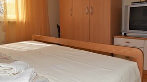 A bedroom with a bed, a wooden wardrobe, a television, and a desk.