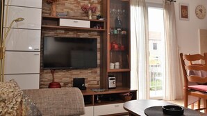 A living room with a flat-screen TV, wooden cabinet, and a dining table with a placemat.