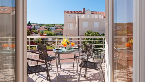 A balcony with wicker chairs, a glass table, and a view of buildings in the background. - Apartments Island Beat - Two Bedroom Apartment with Balcony (A6) (Supetar)