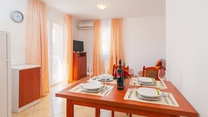 A dining area with a wooden table set for four, a bottle of wine, and a television in the background. - Apartments Island Beat - Two Bedroom Apartment with Balcony (A6) (Supetar)