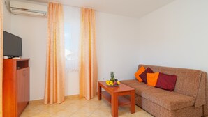 A living room with a sofa, a small table with fruit, a television on a cabinet, and a window with curtains. - Apartments Island Beat - Two Bedroom Apartment with Balcony (A6) (Supetar)