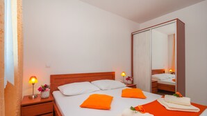 Una habitación de hotel con una cama de madera, dos mesitas de noche con lámparas, un espejo grande y toallas color naranja.