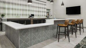 A modern kitchen with a central island, bar stools, a flat-screen TV, and pendant lighting.