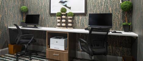 Et moderne kontorrum med to skriveborde, hvert med computer og stol, en printer og dekorative planter.