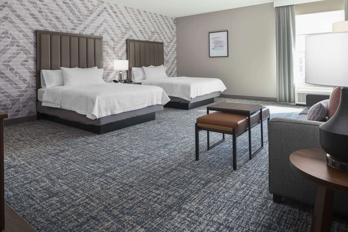 A hotel room with two beds, a sofa, a small table, and a lamp.